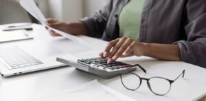 A person organizing receipts and tax documents at a kitchen table with a laptop and calculator.