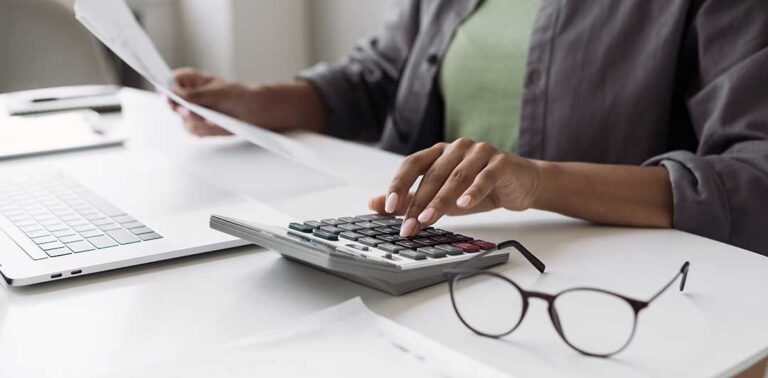A person organizing receipts and tax documents at a kitchen table with a laptop and calculator.