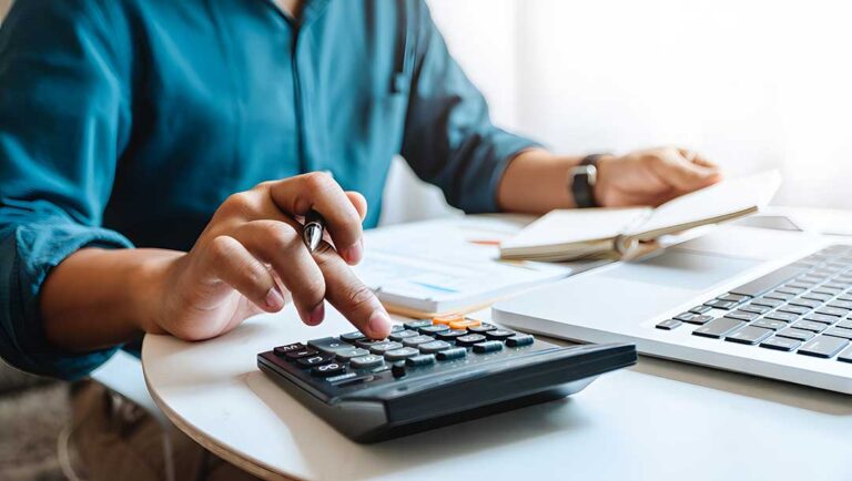 A professional reviews tax forms and financial statements at a desk with a calculator and laptop.