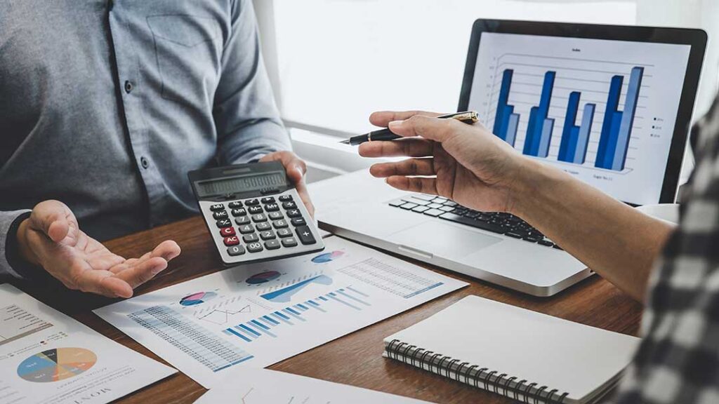 A person reviews a detailed printed pay stub at a kitchen table with a calculator and notepad.