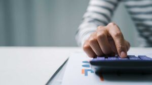 A couple reviews retirement accounts and household expenses at a kitchen table with papers and a calculator.